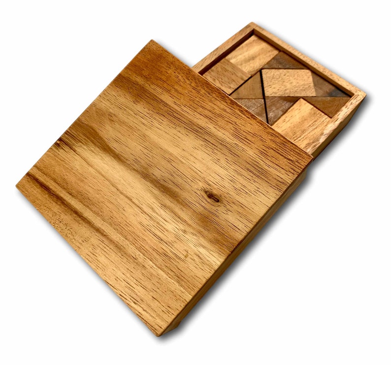 May include: A wooden box with a sliding lid, revealing a wooden puzzle with various geometric shapes. The puzzle pieces are made of light and dark wood, creating a contrasting pattern.