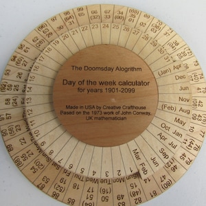 Op de afbeelding: Een ronde houten rekenmachine om de dag van de week te bepalen voor elke datum tussen 1901 en 2099. De rekenmachine is gelabeld met "The Doomsday Algorithm" en "Day of the week calculator for years 1901-2099".