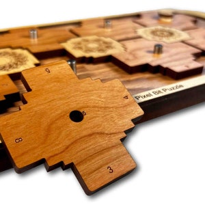 Peut inclure: Une pièce de puzzle en bois avec les chiffres 3, 5, 8 et 9 imprimés dessus. La pièce est en bois brun clair et a un trou au centre. Le texte "Pixel Bit Puzzle" est visible sur le fond.