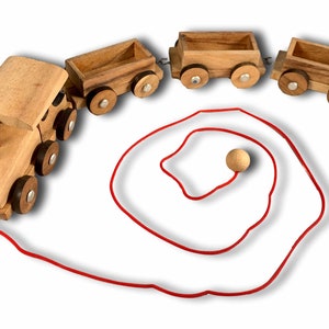 May include: A wooden toy train with four connected cars and a red pull string. The train is made of light brown wood with dark brown wheels and silver accents. The string is coiled.