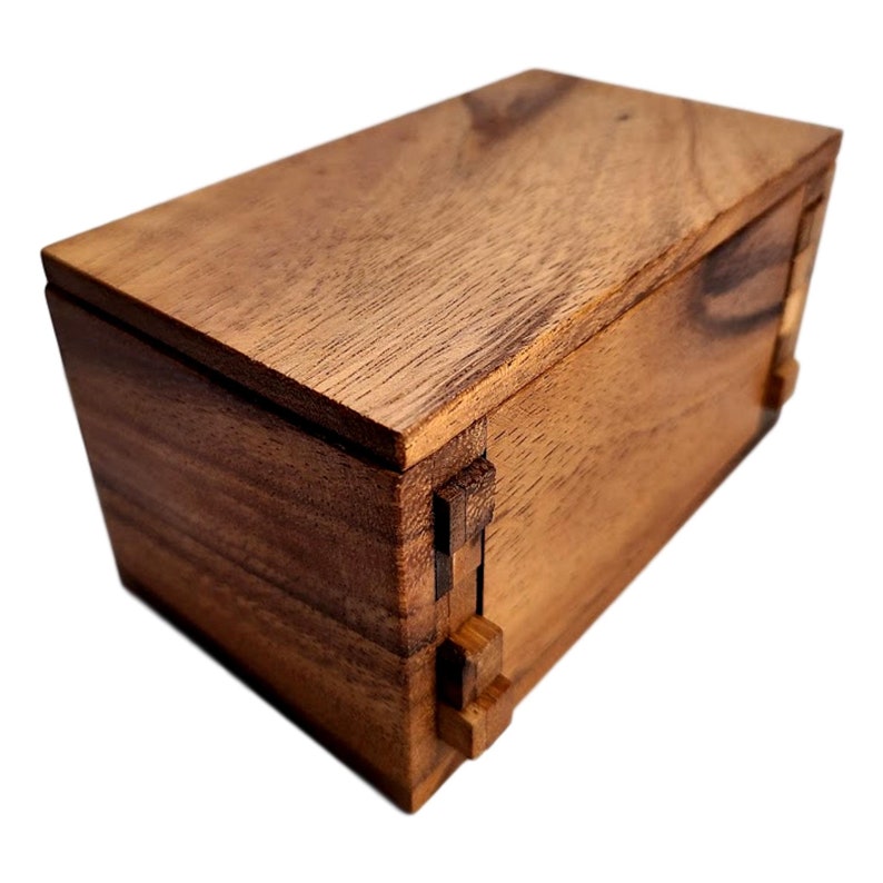 May include: A wooden box with a hinged lid and intricate puzzle-like locking mechanism. The box is made of dark brown wood with a smooth finish.