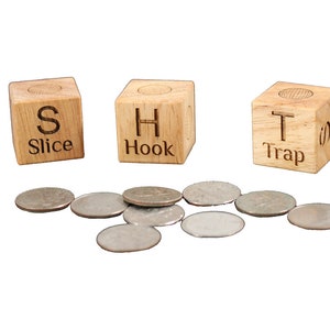 May include: Three wooden blocks with the letters S, H, and T on them. The blocks are labeled "Slice", "Hook", and "Trap". There are several silver coins scattered in front of the blocks.
