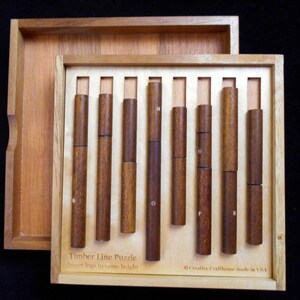 Pode incluir: Uma caixa de madeira com um conjunto de pe&ccedil;as de quebra-cabe&ccedil;a de madeira. A caixa est&aacute; aberta e as pe&ccedil;as est&atilde;o dispostas em uma fileira. A caixa tem o texto "Timber Line Puzzle" e "Insert logs to same height" na frente. A caixa tamb&eacute;m tem o texto "Creative Crafthouse made in USA" na parte inferior.