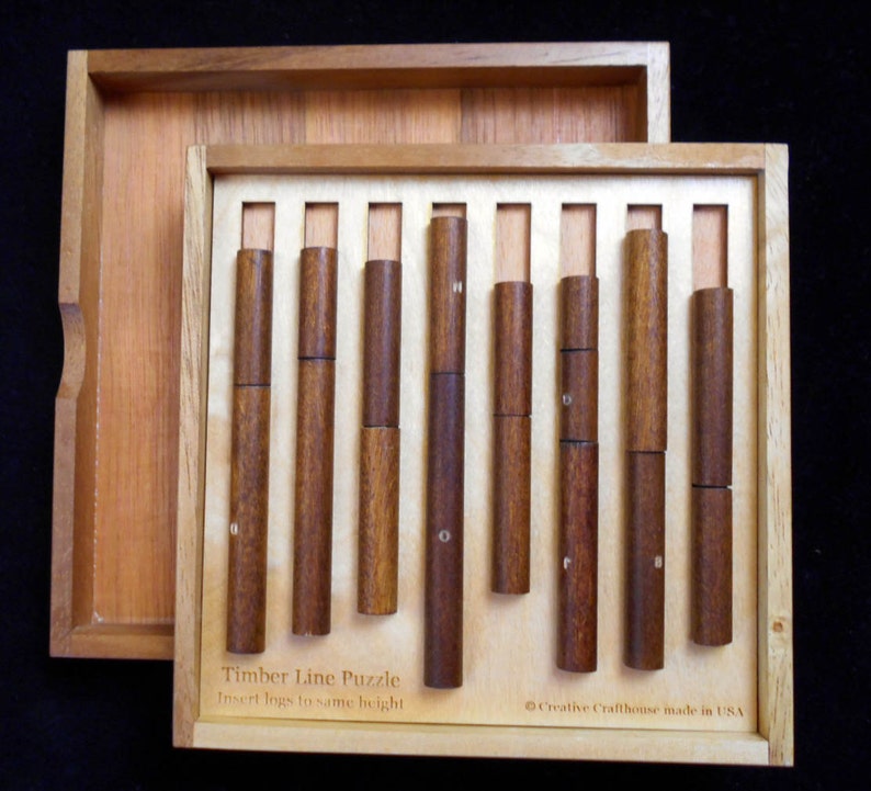 Pode incluir: Uma caixa de madeira com um conjunto de pe&ccedil;as de quebra-cabe&ccedil;a de madeira. A caixa est&aacute; aberta e as pe&ccedil;as est&atilde;o dispostas em uma fileira. A caixa tem o texto "Timber Line Puzzle" e "Insert logs to same height" na frente. A caixa tamb&eacute;m tem o texto "Creative Crafthouse made in USA" na parte inferior.