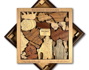 Op de afbeelding: Een houten puzzel met een natuurthema. De puzzel heet "The Hikers Puzzle" en bevat verschillende afbeeldingen die te maken hebben met wandelen, waaronder een kompas, een EHBO-doos, een kaart en twee wandelaars. De puzzel is gemaakt in de VS door Creative Crafthouse.