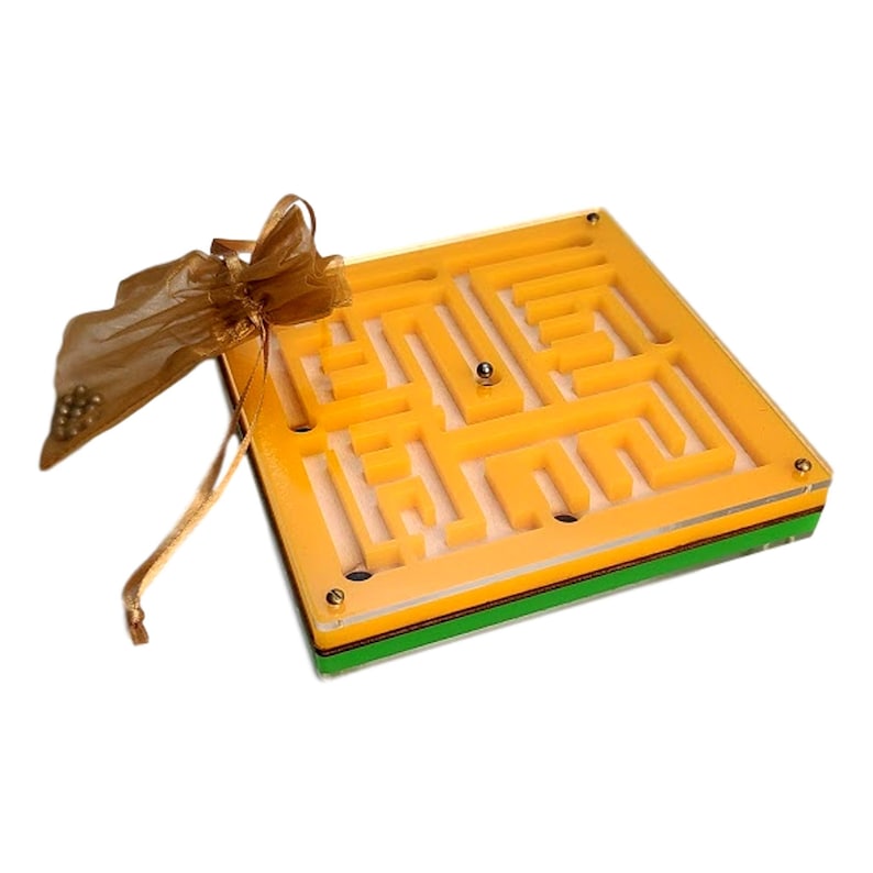 May include: A yellow and clear acrylic maze game with a silver ball inside. The maze is square with a complex path. A small gold drawstring bag filled with small silver balls is next to the maze.
