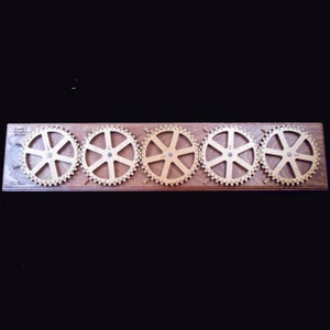 May include: A wooden replica of an Enigma machine with five rotating wheels, each featuring letters and numbers. The wheels are mounted on a wooden base.