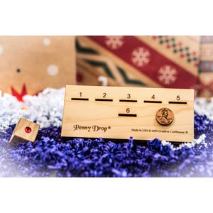 May include: A wooden Penny Drop game with six slots numbered 1 through 6. A penny is in the slot labeled 6. The game is made in the USA by Creative Crafthouse.