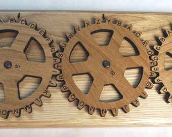 Puede incluir: Una máquina de encriptación Enigma II de madera con tres engranajes rotativos. Cada engranaje tiene un alfabeto diferente impreso en él. Los engranajes están etiquetados con los números 70, 60 y 19. La máquina está hecha en los Estados Unidos por Creative Crafthouse.