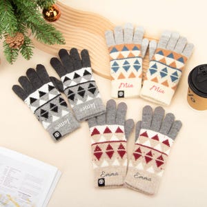 Peut inclure: Plusieurs paires de gants d'hiver tricotés, de couleurs grises, crème et bordeaux. Chaque paire présente un motif géométrique et un nom brodé. Les noms "James", "Mia" et "Emma" sont visibles sur certains gants.