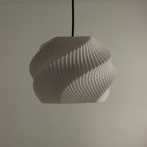 Pode incluir: Uma luminária pendente branca e geométrica com uma superfície texturizada. A lâmpada é suspensa por um cabo preto e tem um design espiralado único. Esta luminária é um item de decoração moderna.