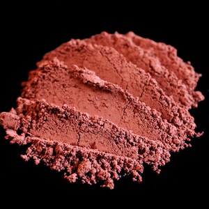 May include: Close-up of a pile of red powder, likely a natural pigment or cosmetic, against a black background.