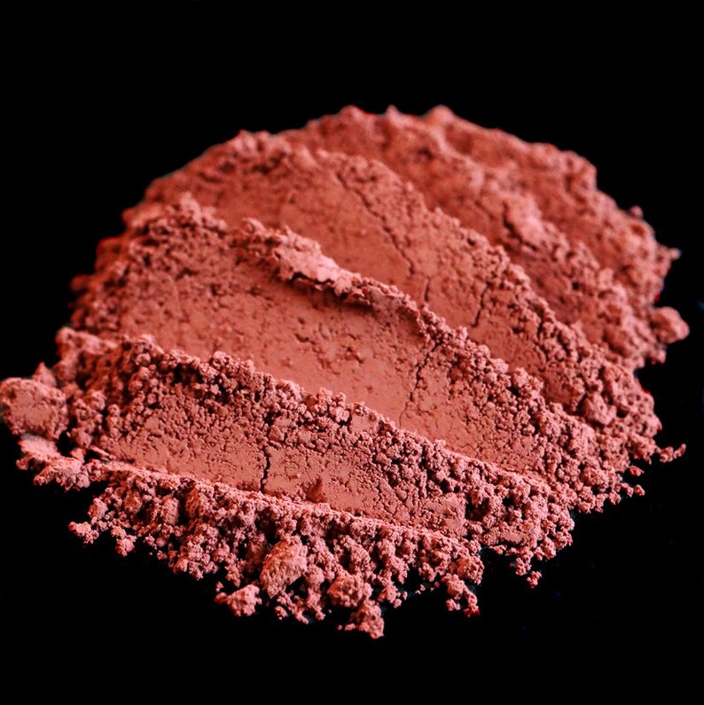 May include: Close-up of a pile of red powder, likely a natural pigment or cosmetic, against a black background.