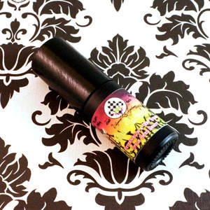 Op de afbeelding: Een zwarte en zilveren roll-on fles met een kleurrijk etiket waarop "Gour Sucker" en "Watermelon & Tangerine with a hint of Green Apple" staat.