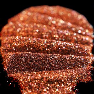 May include: Close-up of a pile of shimmering copper glitter. The glitter is arranged in a wave-like pattern, creating a textured and sparkly effect.