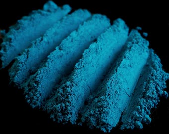 May include: Close-up of a pile of blue powder, arranged in parallel lines, against a black background.