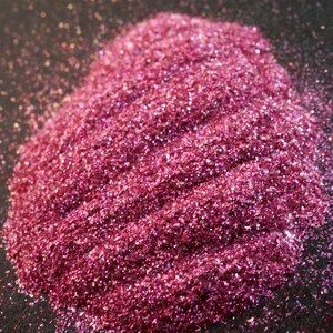 Puede incluir: Primer plano de un montón de purpurina rosa con brillo iridiscente. La purpurina es fina y tiene una superficie ligeramente texturizada.
