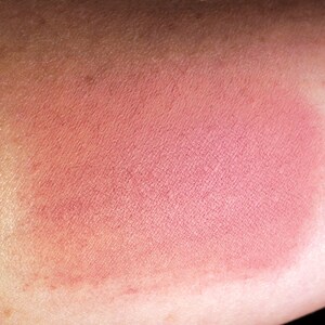 May include: A close-up of a pink blush applied to skin. The blush has a smooth, matte finish.