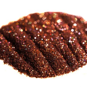 May include: A close-up of a pile of iridescent copper glitter. The glitter is arranged in a wave-like pattern, creating a shimmering effect.