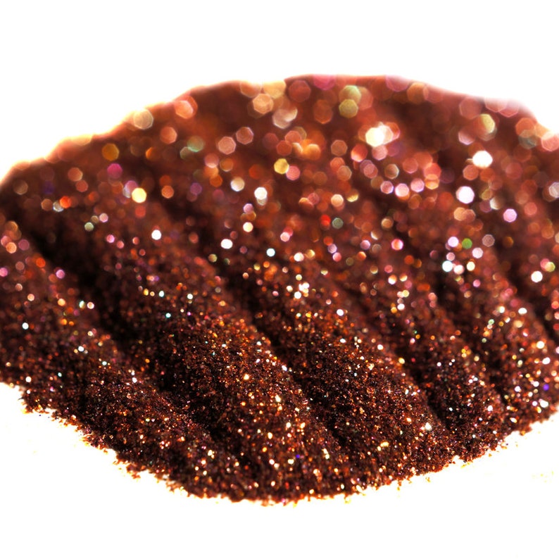 May include: A close-up of a pile of iridescent copper glitter. The glitter is arranged in a wave-like pattern, creating a shimmering effect.