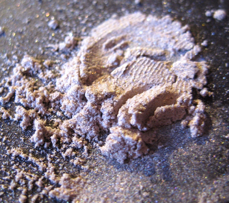 Pu&ograve; includere: Primo piano di un mucchio di glitter sciolto di colore viola chiaro con una finitura scintillante. Il glitter &egrave; sparso su una superficie grigio scuro.