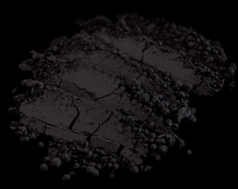 May include: A close-up of a pile of black powder, showing the texture and fine particles. The powder is spread out on a black background.