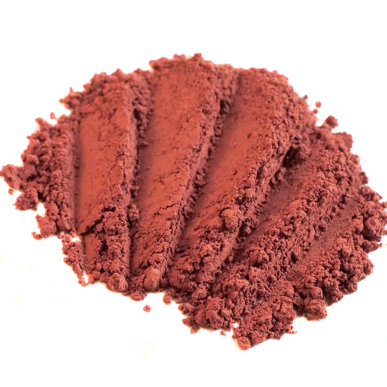 May include: A close-up of a pile of red-brown powder. The powder is finely ground and has a smooth, even texture.