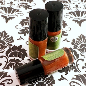 May include: Three small bottles of shimmery orange nail polish with black caps and green labels. The bottles are on a white background with a black and white floral pattern.