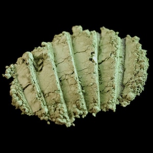 May include: A close-up of a green powder, possibly matcha, arranged in a swirl pattern on a black background.