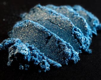 May include: Close-up of a pile of blue glitter eyeshadow. The glitter is fine and has a shimmery finish.