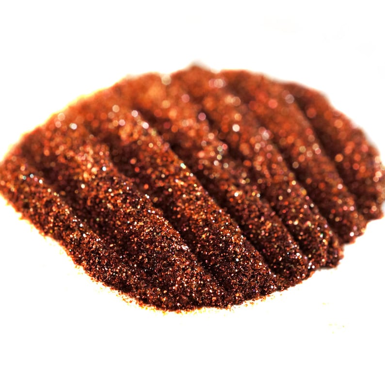 May include: A close-up of a pile of fine, sparkly copper glitter. The glitter is arranged in a wave-like pattern, creating a shimmering effect.