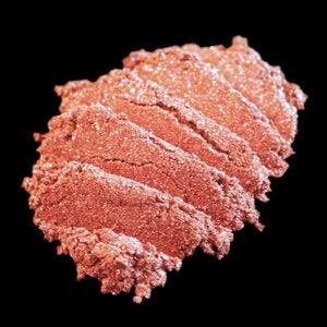 May include: A close-up of a pile of loose, shimmery, peach-coloured eyeshadow. The eyeshadow has a fine, glittery texture.