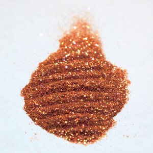 May include: A pile of copper glitter with iridescent shimmer. The glitter is spread out on a white surface.