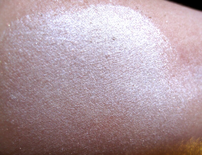 Pu&ograve; includere: Primo piano di un ombretto bianco shimmer, che mostra la sua texture e la finitura perlata.