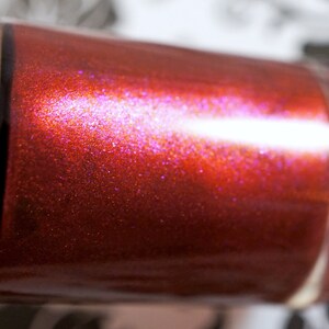 Puede incluir: Primer plano de una botella de esmalte de uñas rojo con un acabado brillante e iridiscente.