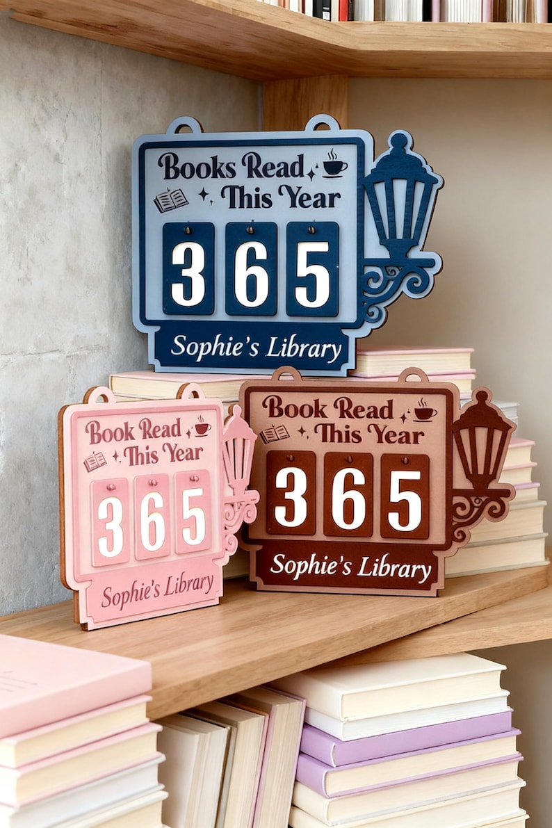Peut inclure: Trois compteurs de livres en bois bleus, roses et marron, affichant chacun "Livres lus cette ann&eacute;e" et le nombre "365". Les compteurs ont un motif de lanterne et le texte "Sophie's Library".