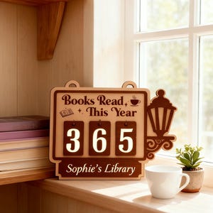 Peut inclure: Panneau en bois avec le texte "Books Read This Year" et le chiffre "365". Le panneau comprend &eacute;galement le texte "Sophie's Library". Une tasse &agrave; caf&eacute; blanche et une petite plante en pot sont pos&eacute;es sur un rebord de fen&ecirc;tre en bois.