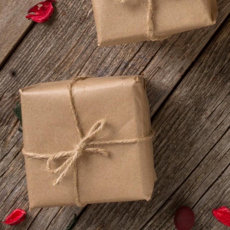 May include: Two square gifts wrapped in brown paper and tied with twine, arranged on a rustic wooden surface. Red decorative accents are scattered around the gifts, adding a pop of color to the scene. The gifts are ready to be given.