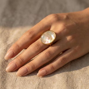 Anillo ovalado de nácar, banda ajustable en tono dorado, joyería minimalista para uso diario.