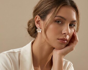 May include: A white flower-shaped stud earring with five rounded petals and a small central accent. The earring is crafted with a smooth, matte finish and features a post-back closure, providing a clean and simple look for the earlobe.