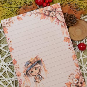 Könnte beinhalten: Ein rechteckiges Blatt liniertes Briefpapier mit pfirsichfarbenem Hintergrund. Der Rand ist mit herbstlichen Illustrationen verziert, darunter orangefarbene Ahornblätter, weiße Gänseblümchen, rote Beeren und eine kleine Figur mit Hut.