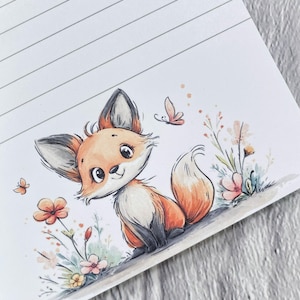 Könnte beinhalten: Eine bezaubernde Illustration eines Fuchswelpen mit orangefarbenem und weißem Fell, umgeben von Blumen und Schmetterlingen. Das Kunstwerk befindet sich auf einem linierten Notizblock, ideal für Notizen oder Skizzen. Der Fuchs hat große, ausdrucksstarke Augen.
