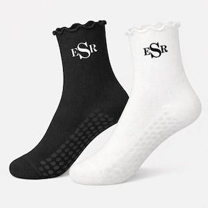 May include: A pair of socks, one black and one white, with a ruffled top edge. Each sock features the letters "ESR" in black. The soles have a dotted pattern for grip.