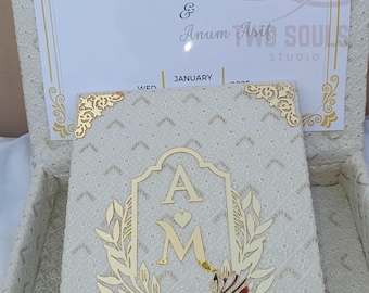 May include: A cream-coloured wedding invitation set. The card reads "They Decided on Forever!" with names and "January". The invitation has gold detailing and a monogram with the initials "A" and "M". The box and card are decorated with a floral pattern.