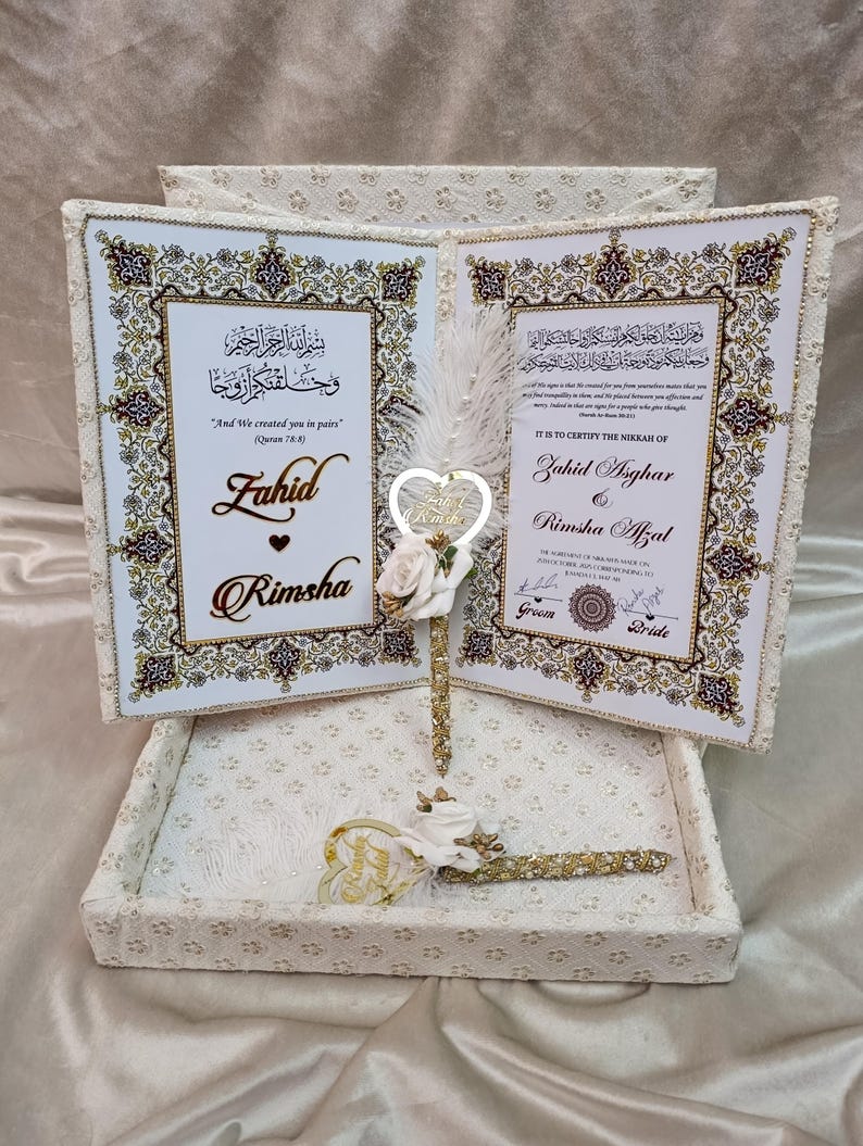 May include: A wedding gift set with two open books, featuring gold and white ornate frames. The books display text in Arabic and English, with the names Zahid and Rimsha. A heart-shaped ornament and a pen are included.