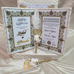 May include: Wedding certificate set with two framed documents, gold detailing, and decorative borders. The set includes a pen with a heart-shaped embellishment and white roses. The certificates feature Arabic script and names, perfect for a special occasion.