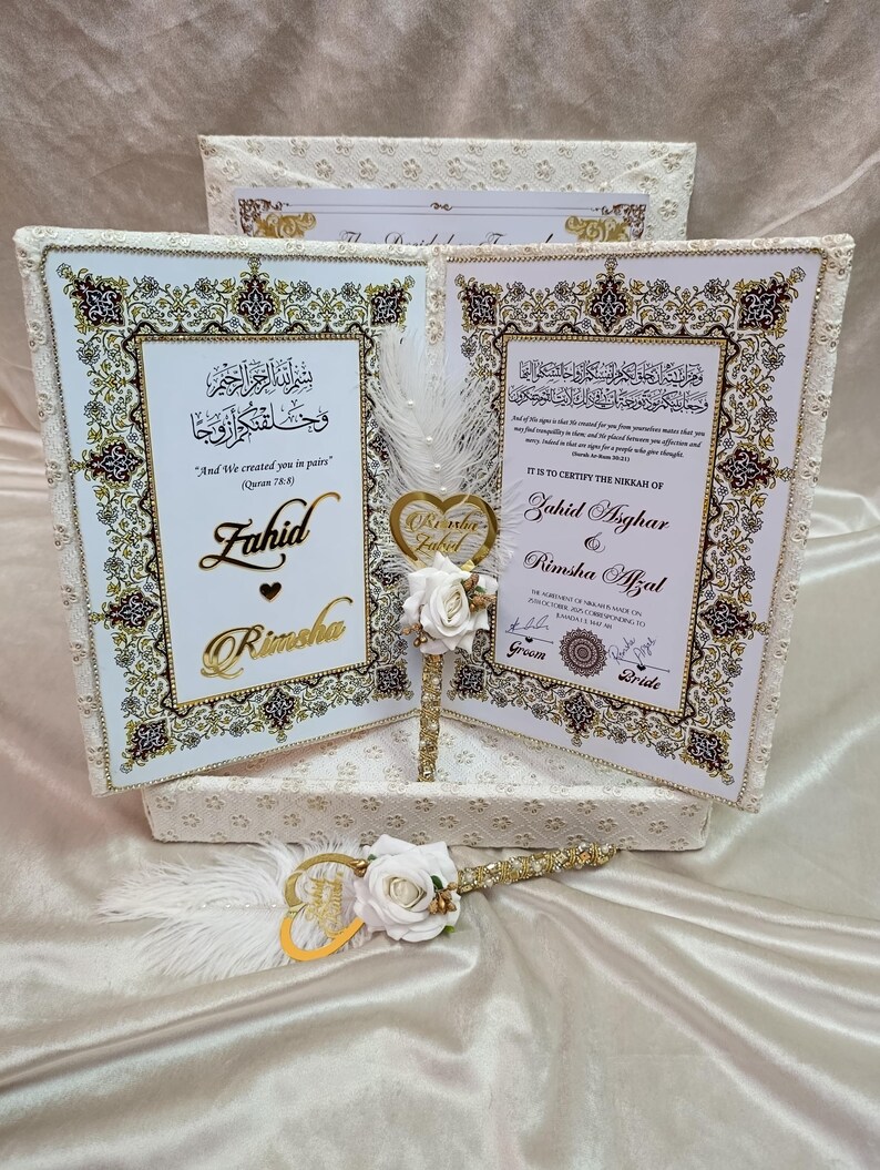 May include: Wedding certificate set with two framed documents, gold detailing, and decorative borders. The set includes a pen with a heart-shaped embellishment and white roses. The certificates feature Arabic script and names, perfect for a special occasion.