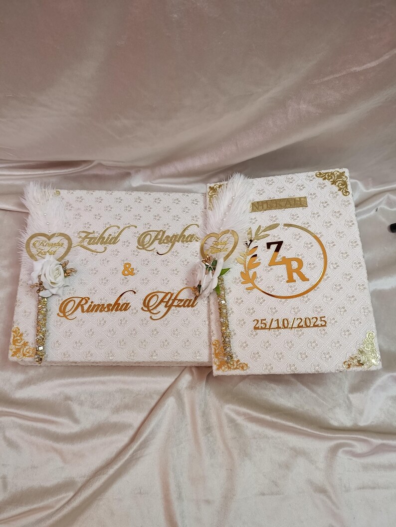 May include: Two white wedding guest books with gold detailing. The left book features the names "Fahid Asgha" and "Rimsha Afzal" in gold script. The right book has the word "Nikkah" and the date "25/10/2025".