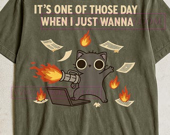 Op de afbeelding: Olijfgroen t-shirt met een cartoonkat die een vlammenwerper op een laptop gebruikt, omringd door brandende papieren. De tekst op het shirt luidt "IT'S ONE OF THOSE DAY WHEN I JUST WANNA".