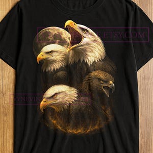 Könnte beinhalten: Schwarzes T-Shirt mit einer detaillierten Illustration von vier Adlerköpfen. Das Design umfasst einen Vollmondhintergrund und ein feuriges Leuchten am unteren Rand. Das Etsy.com-Logo ist sichtbar. Die Adler haben offene Schnäbel und stechende Augen.